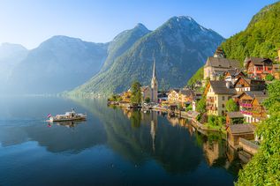 Klassischer Panoramablick auf die berühmte Altstadt von Hallstatt und den tiefblauen Alpensee mit Touristenschiff im malerischen goldenen Morgenlicht an einem wunderschönen sonnigen Tag bei Sonnenaufgang im Sommer, Salzkammergut, Österreich