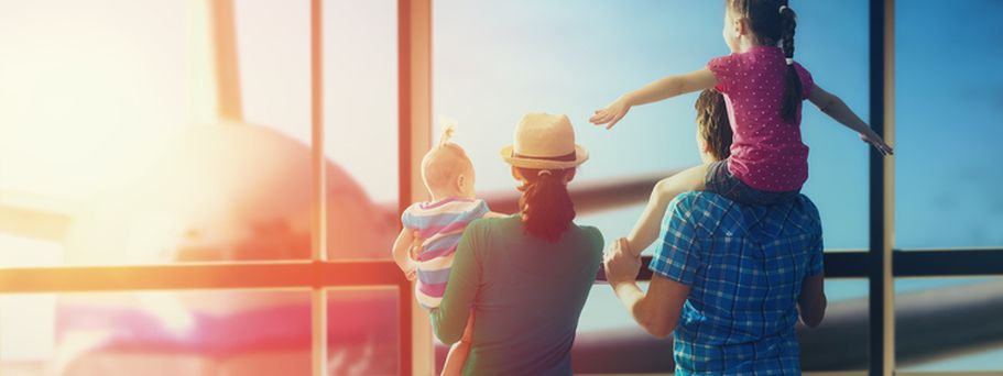 Familie mit zwei kleinen Kindern steht am Flughafenfenster und schaut auf ein Flugzeug bei Sonnenuntergang.