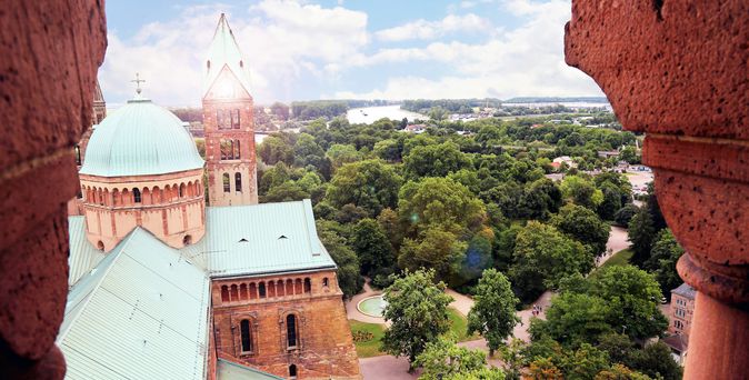 Blick auf den Dom zu Speyer mit seinen markanten Türmen und grünen Kupferdächern, eingerahmt von Bäumen und Parklandschaft.