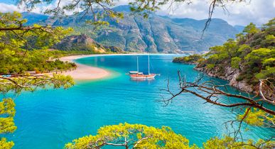 Atemberaubender Blick auf die Blaue Lagune von Ölüdeniz, Türkei, mit einem Segelboot im türkisblauen Wasser, umgeben von grünen Bergen und Pinienwäldern.