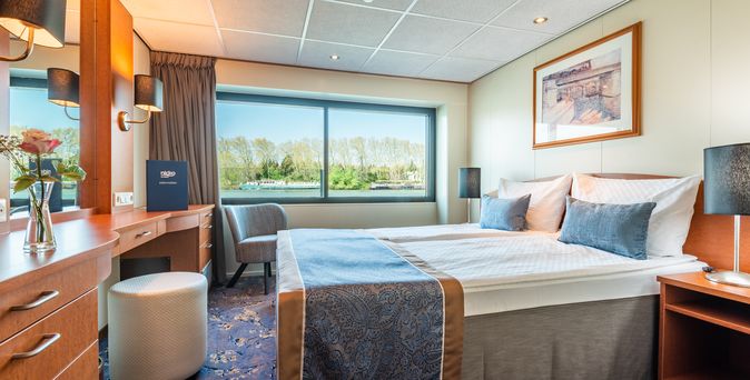 Eine luxuriöse Schiffskabine mit einem großen Bett und Blick nach draußen.