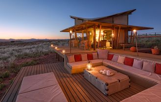 Modernes, beleuchtetes Glamping-Zelt bei Sonnenuntergang, umgeben von Bäumen.
