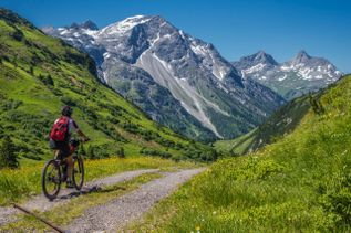 Ein Mountainbiker fährt einen Pfad hinauf, mit Bergen im Hintergrund.