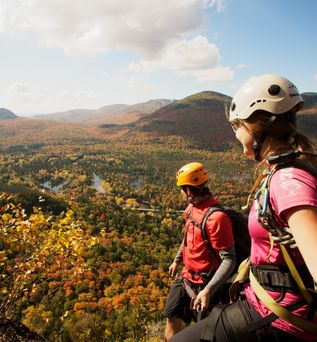 Wanderer mit Helmen blicken von oben auf eine herbstlich gefärbte Hügellandschaft