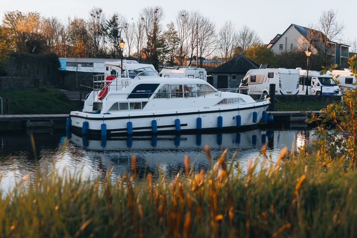 Ein kleines, weißes Motorboot mit dem Schriftzug "CARRICKCRAFT" und blauen Akzenten, das auf einem ruhigen Fluss oder See fährt. Im Hintergrund ist eine bewaldete Uferlandschaft mit weiteren Booten zu sehen.