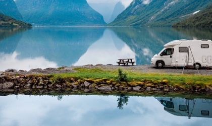 Weißer Campervan steht auf einer kleinen Landzunge im See, umgeben von Bergen und Wasser.