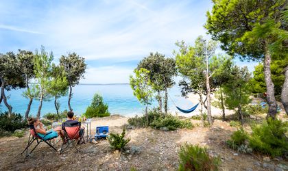 Campingplatz in Kroatien mit Zelten und Campervans am Wasser, umgeben von Bäumen.