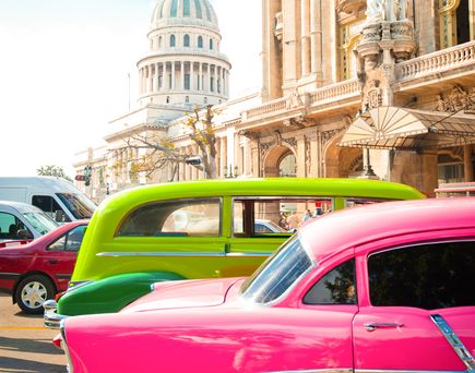Ein pinkfarbener Oldtimer vor einem historischen Gebäude.
