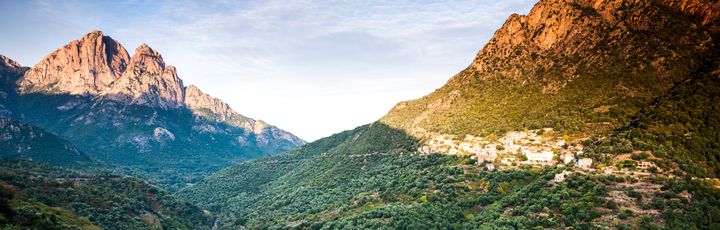 Eine weite Berglandschaft mit einem See oder Fjord, der sich in den Bergen spiegelt, unter einem klaren blauen Himmel.