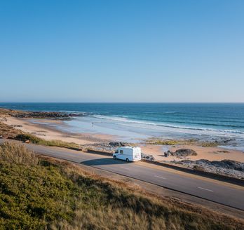 Camper fährt entlang einer Küstenstraße am Meer mit felsigem Strand 