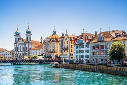 Blick auf Luzern an der Waterfront des Vierwaldstättersees. Kleine geschmackvolle Häuser, Gebäude mit Kirchtürmen und strahlend blauer Himmel.