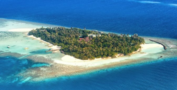 Eine Luftaufnahme einer Insel mit einem Resort und türkisfarbenem Wasser.