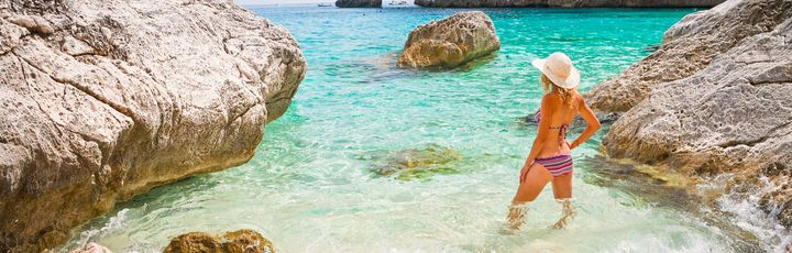 Ein Sandstrand mit türkisfarbenem Wasser und einer Person.