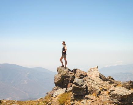 Eine Frau steht auf dem Gipfel und blickt auf den Horizont