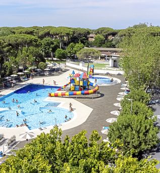Wasserpark mit mehreren Pools, bunter Wasserburg und zahlreichen Sonnenschirmen inmitten eines bewaldeten Ferienparks.