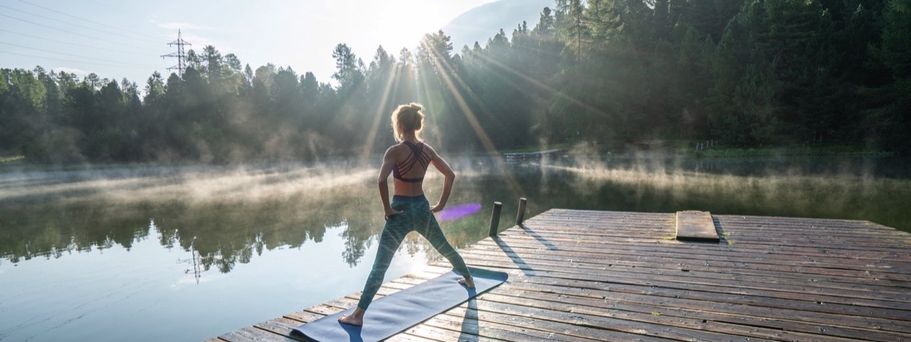Eine Person macht Yoga auf einem Steg an einem See bei Sonnenuntergang.