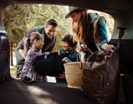 Eine Familie packt Campingausrüstung in ein Wohnmobil, Kinder helfen mit.
