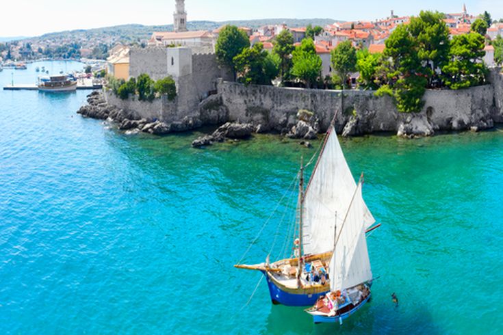 Ein Segelboot im Hafen von Krk, Kroatien, mit der Altstadt im Hintergrund.