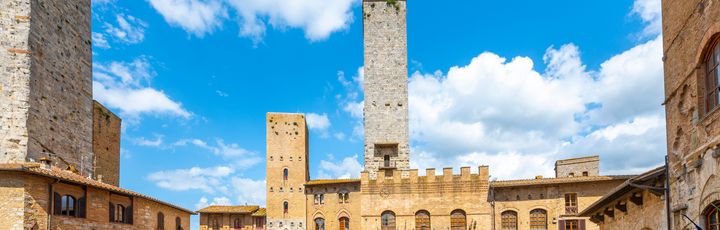 Touristen an einem Sommertag unter blauem Himmel vor der Torre Rognosa und den Salvucci-Türmen auf der Piazza Duomo in der historischen toskanischen Bergstadt San Gimignano