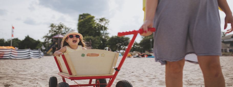 Ein Kind zieht einen Bollerwagen am Strand.
