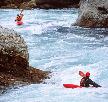 Ein Schlauchboot mit Personen auf einem Fluss, umgeben von Stromschnellen.