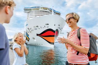 FAmilie freut sich , steht an LAnd im Hintergrung steht ein AIDA Schiff