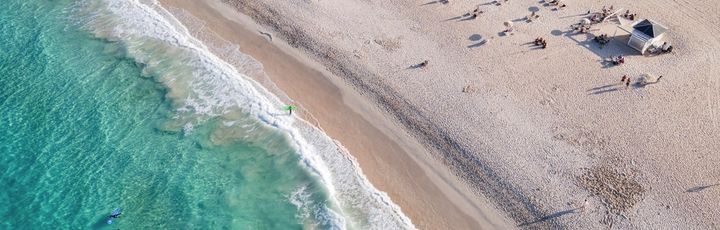 Ein Sandstrand mit Dünen und blauem Meer.