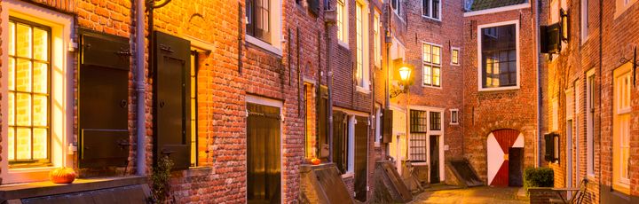 Eine enge Gasse in einer Stadt bei Nacht, mit beleuchteten Gebäuden.