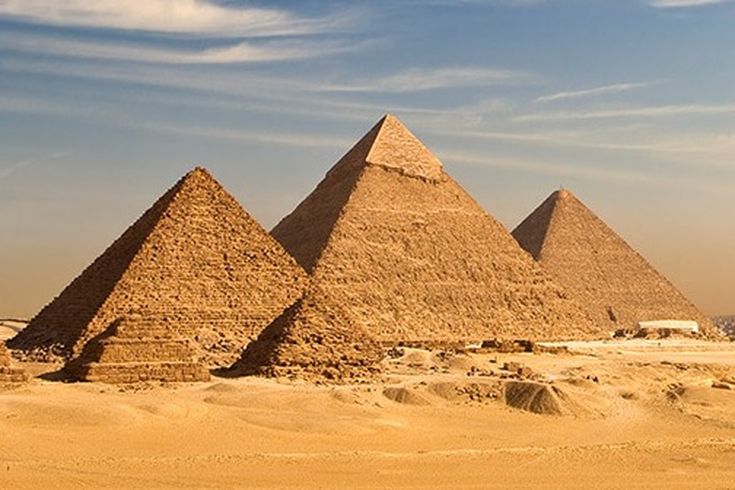 Weitläufiges Wüstenpanorama mit den eindrucksvollen Pyramiden von Gizeh vor der nahen Skyline Kairos.