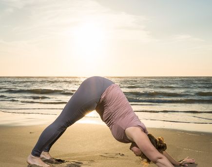 Eine Person macht Yoga am Strand bei Sonnenuntergang.