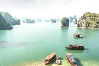 Eine malerische Bucht in Vietnam mit zahlreichen Kalksteininseln und mehreren Booten, darunter einige Kajaks am Ufer.