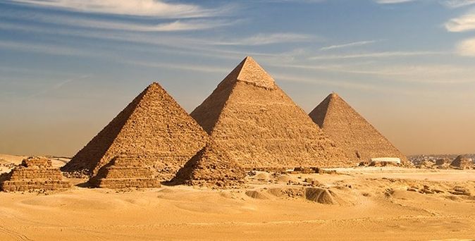 Weitläufiges Wüstenpanorama mit den eindrucksvollen Pyramiden von Gizeh vor der nahen Skyline Kairos.