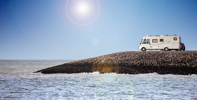Weißer Camper steht auf Felsspitze mit Blick auf die See. Blauer Himmel mit strahlender Mittagssonne.