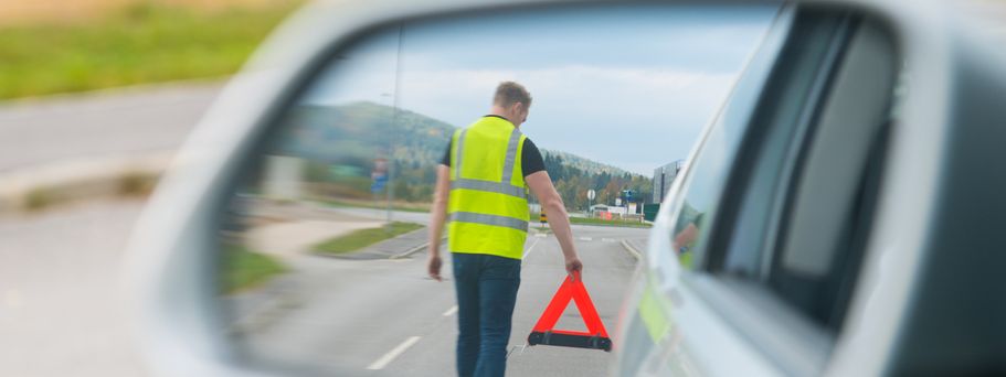 Ein Rückspiegel eines Autos zeigt eine Person, die einen Warnkegel aufstellt.