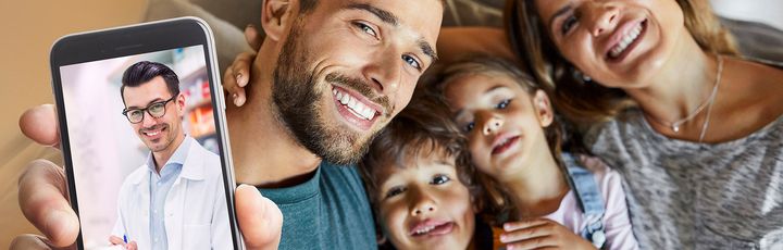 Glückliche Familie auf dem Sofa zeigt einen digitalen Arztbesuch per App auf dem Smartphone – moderne Gesundheitsversorgung von überall.