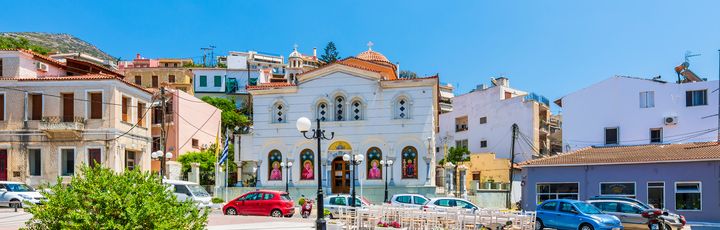 Blick auf die Innenstadt von Vathy mit seinen kleinen bunten Häuser, Sitzmöglichkeiten und einigen Autos.