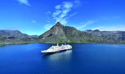 Ein Kreuzfahrtschiff in einem Fjord mit einem Vulkan im Hintergrund.