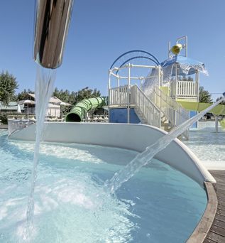 Kinderfreundlicher Wasserpark mit Rutschen, Wasserspielen und flachem Poolbereich unter blauem Himmel.