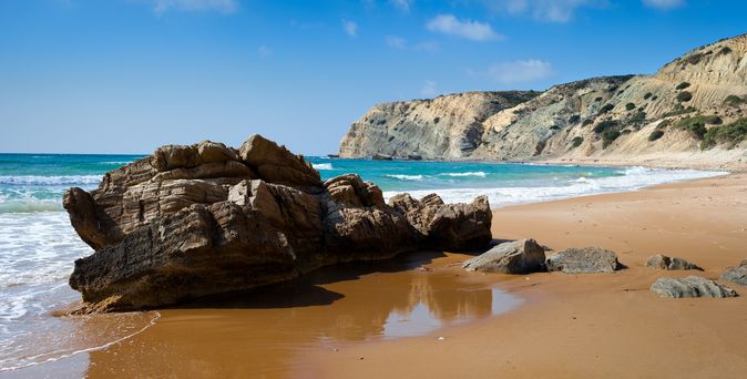 Ein Sandstrand mit Felsen und Meer.