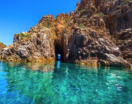 Die beeindruckenden roten Felsformationen der Calanques de Piana in Korsika, Frankreich, die steil aus dem türkisblauen Meer aufragen, umgeben von üppiger Vegetation.