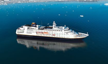 Ein großes weißes Kreuzfahrtschiff fährt auf ruhigem Wasser, umgeben von eisiger Landschaft.