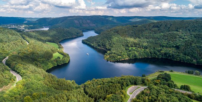 Eine Luftaufnahme zeigt den Obersee im Nationalpark Eifel, umgeben von dichten grünen Wäldern und Hügeln.