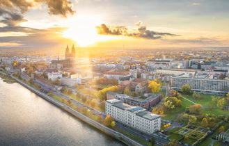 Eine Stadtansicht bei Sonnenuntergang mit einem Fluss und beleuchteten Gebäuden.