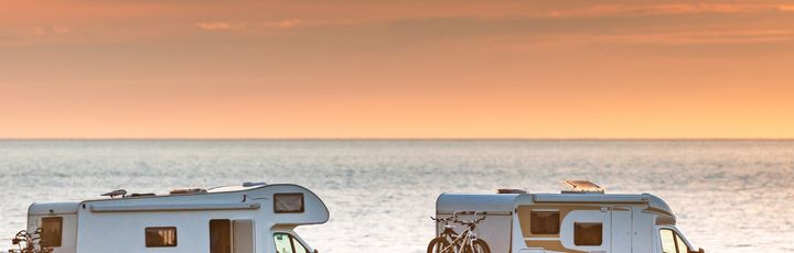 Weißer Campervan steht an einem Fjordufer in Norwegen bei Sonnenuntergang, umgeben von Bergen.