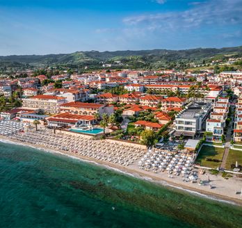 Blick auf Hanioti aus der Vogelperspektive. Breiter Strand mit Liegen, dahinter Grün und Häuser.