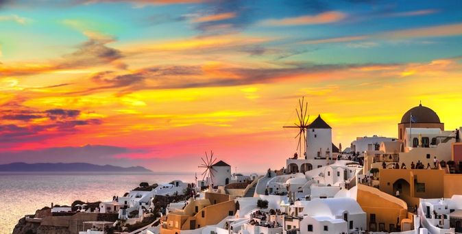 Eine Stadtansicht von Santorini, Griechenland, mit weißen Häusern und blauen Kuppeln bei Sonnenuntergang.