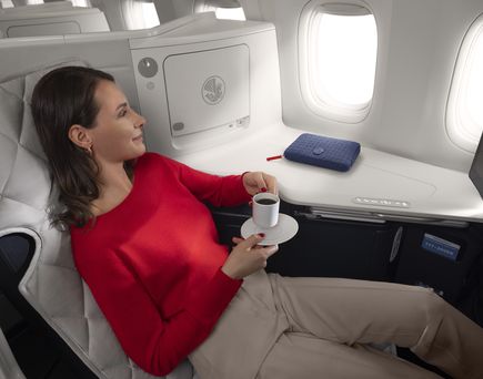 Frau mit Tasse sitzt in Business Class im Flugzeug