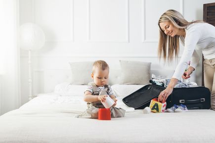Frau packt koffer und Baby sitzt davor auf dem Bett