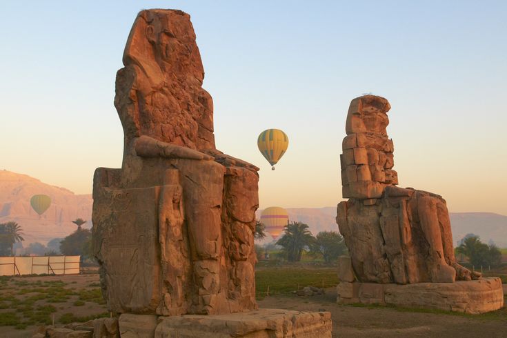 Die zwei kolossalen Statuen der Memnonkolosse, die majestätisch in der Landschaft stehen und die Überreste eines antiken Tempels markieren.