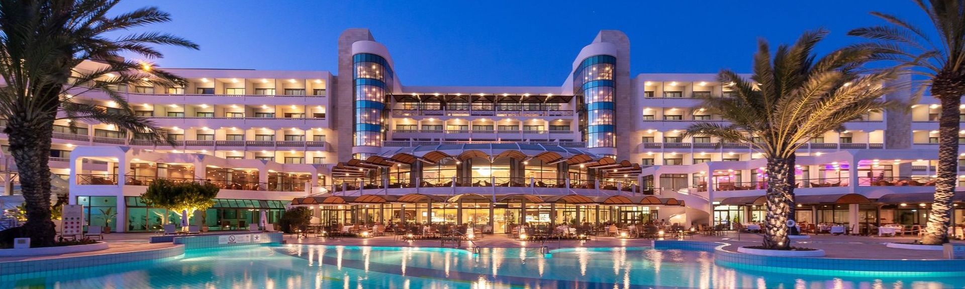 Constantinou Bros Athena Beach Hotel in der Abenddämmerung. Schön beleuchtet mit Lichtreflektionen im Pool
